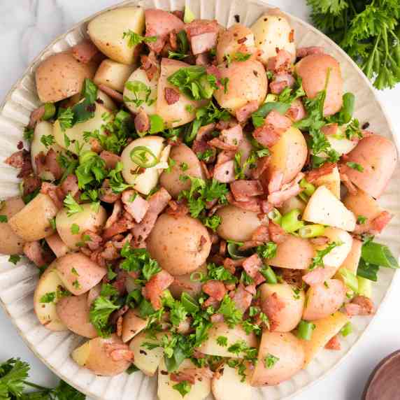 View of a platter full of cooked red potatoes, bacon pieces, green onions and parsley from above.