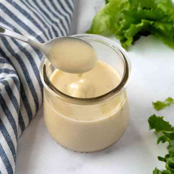 Yogurt Honey Mustard Dressing in a glass jar and a spoon on a white countertop.
