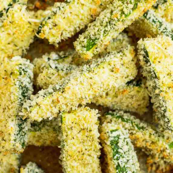 Breaded baked zucchini fries piled on a baking sheet. 