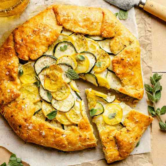 A zucchini galette with a wedge cut out and a knife to the side on parchment. 