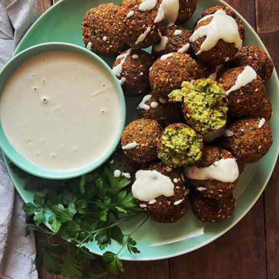 green plate stacked with zucchini and sesame falafels with tahini dressing 