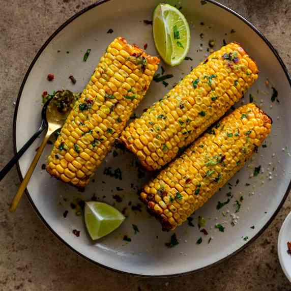 3 corn on the cob topped with coriander on a round beige plate