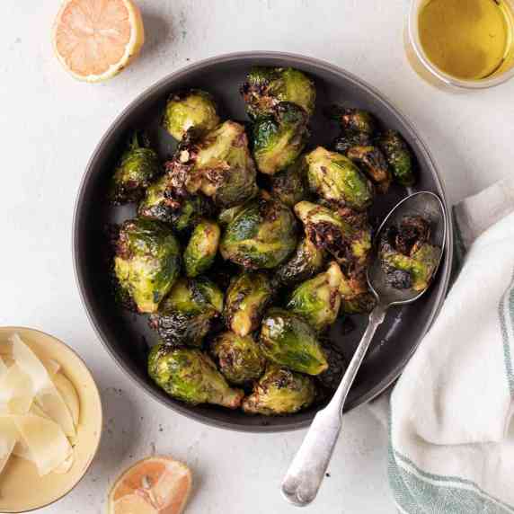 Smashed brussels sprouts in a dark grey round bowl with a large spoon.