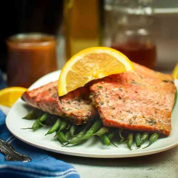 Side shot of two salmon filets garnished with an orange slice on a bed of green beans on a plate. 