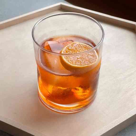 an orange tinted aperol negroni in a rocks glass with orange slice