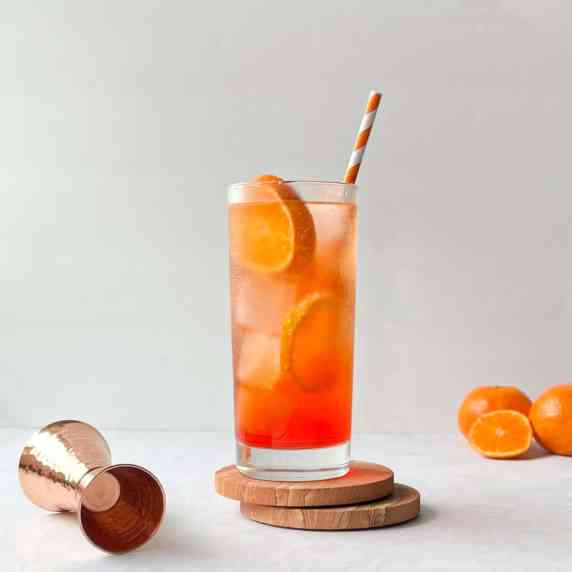 orange highball aperol soda garnished with orange slices and a orange striped straw.