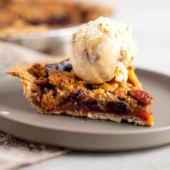 A slice of apple blueberry pie topped with a scoop of ice cream. 