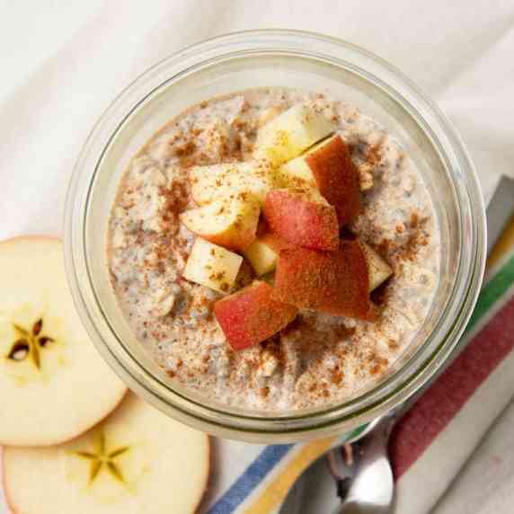Top view of a glass jar of apple cinnamon overnight oats garnished with chopped apples and cinnamon.