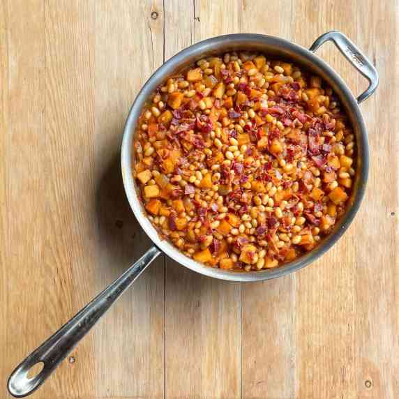 frying pan filled with beans, apple pie filling, and topped with bacon bits.