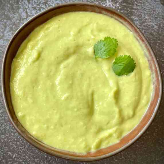 Bowl of vegan avocado crema, garnished with cilantro.