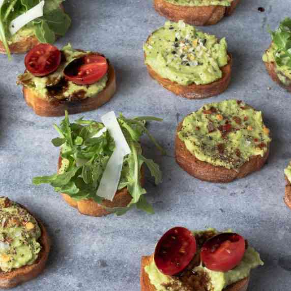 A platter of avocado crostini with assorted toppings.