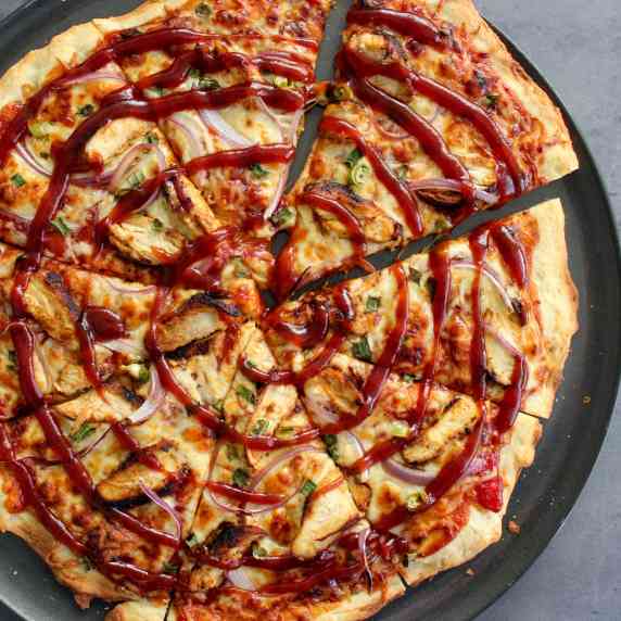 A thin crust BBQ chicken pizza sliced in 8 triangles and topped with extra barbecue sauce