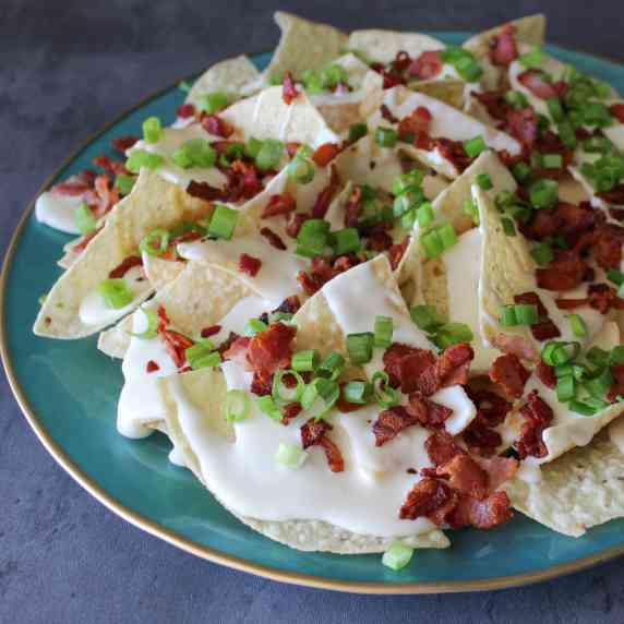 A plate of nachos topped with creamy beer cheese, bacon bits, and scallions.