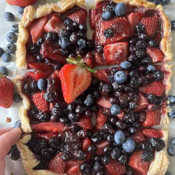 a blueberry and strawberry puff pastry with a piece  being picked up by a hand