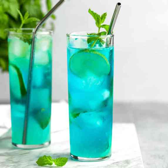 Blue mojitos garnished with lime slices and mint leaves, on a white background. 