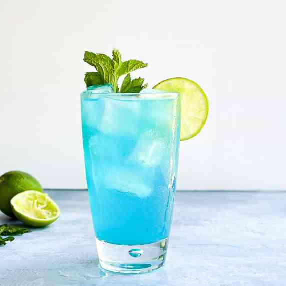 pale blue cocktail in a tall glass with ice garnished with lime and mint.