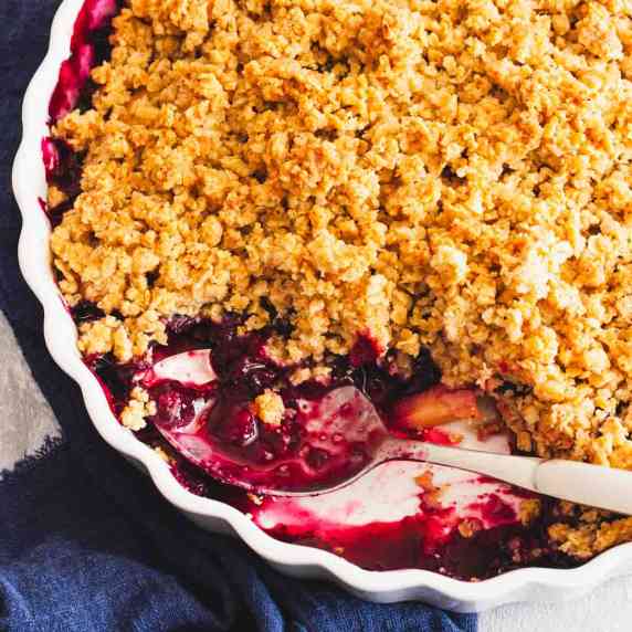 Blueberry apple crumble in a white baking dish with a spoon.