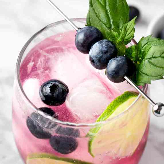 A blueberry mojito mocktail garnished with blueberries and lime wheels.