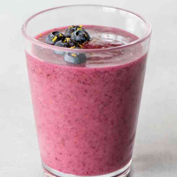 A lemon blueberry smoothie topped with fresh blueberries and lemon zest in a tall glass.