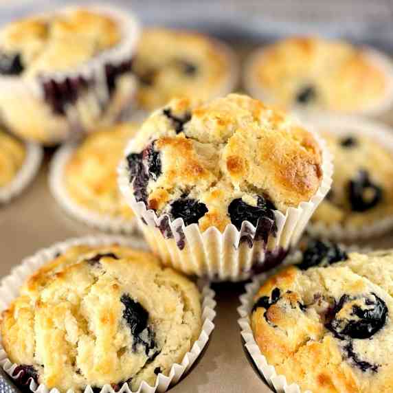 blueberry muffins sitting in a muffin tin with one sitting on top.