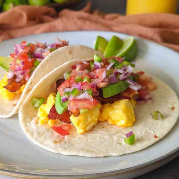 Two breakfast tacos of scrambled eggs, bacon, avocado, and pico de gallo on a plate