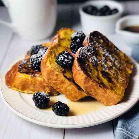 brioche French toast stacked up on a plate with honey drizzled over top