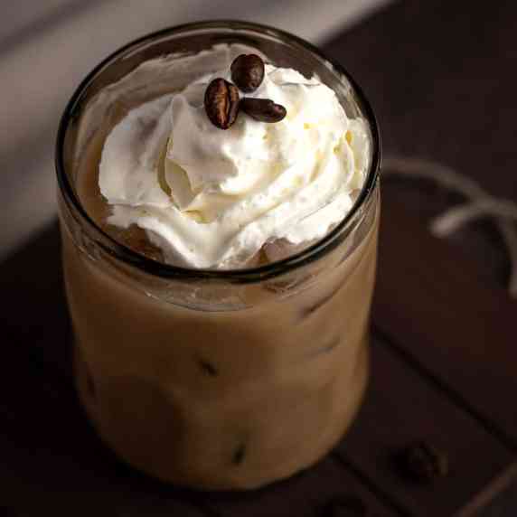 A brown cow drink topped with whipped cream and 3 coffee beans. 