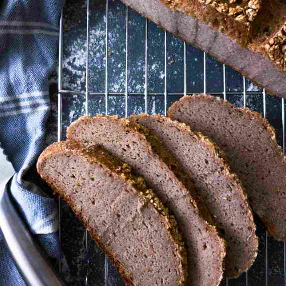 buckwheat bread sliced on a cooling rack with a loaf in the background.