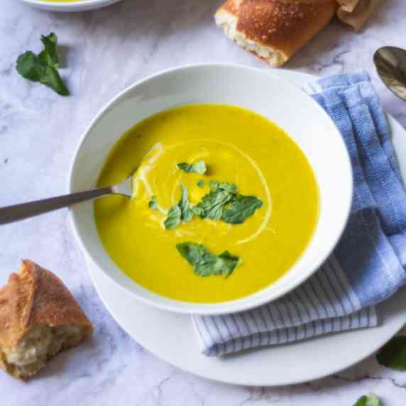 Bowl of butternut squash and broccoli soup with crusty bread next to it. 
