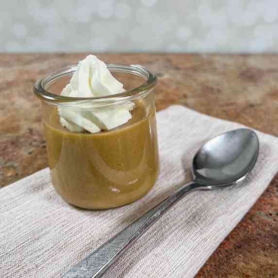 Butterscotch pudding topped with whipped cream on a light brown napkin with a spoon.