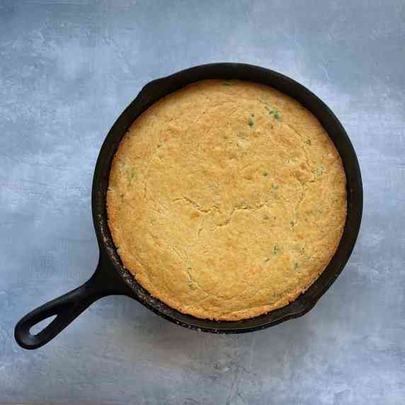brown butter cornbread in a cast iron pan on a blue countertop.