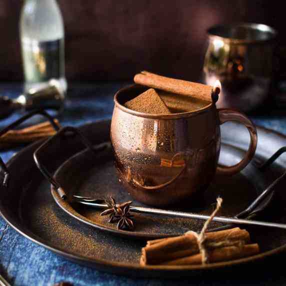 Moscow mule in a copper mug on a silver tray with cinnamon sticks.
