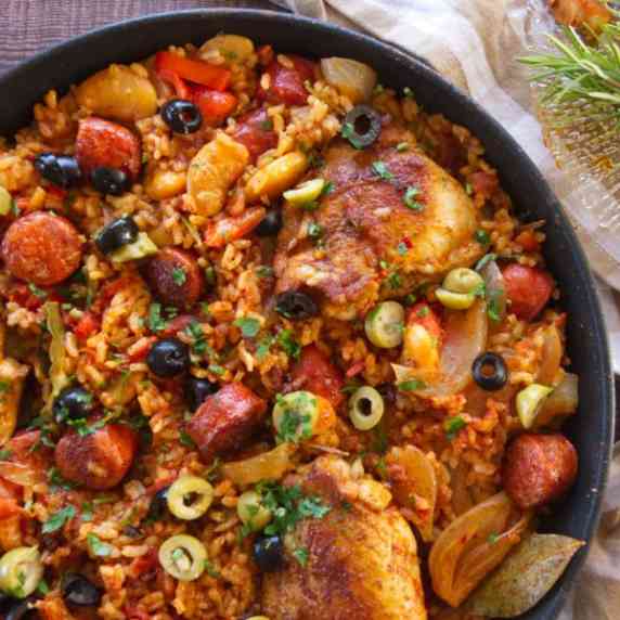 a large pan of arroz con pollo garnished with olives and fresh parsley
