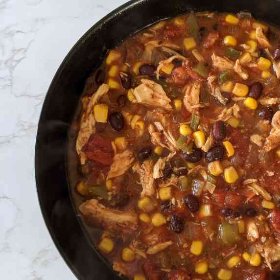A bowl of chicken tortilla soup with black beans, corn, tomato, and green chiles.