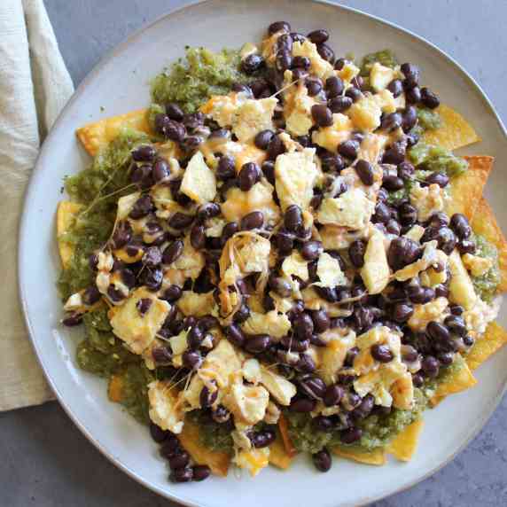 A plate of green chilaquiles topped with cheesy scrambled eggs and black beans.