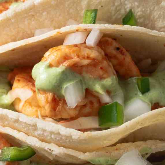 Close up of a shrimp taco topped with green sauce, jalapenos, and onions.