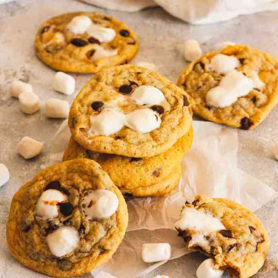 A stack of chocolate chip marshmallow cookies on parchment paper next to mini marshmallows.