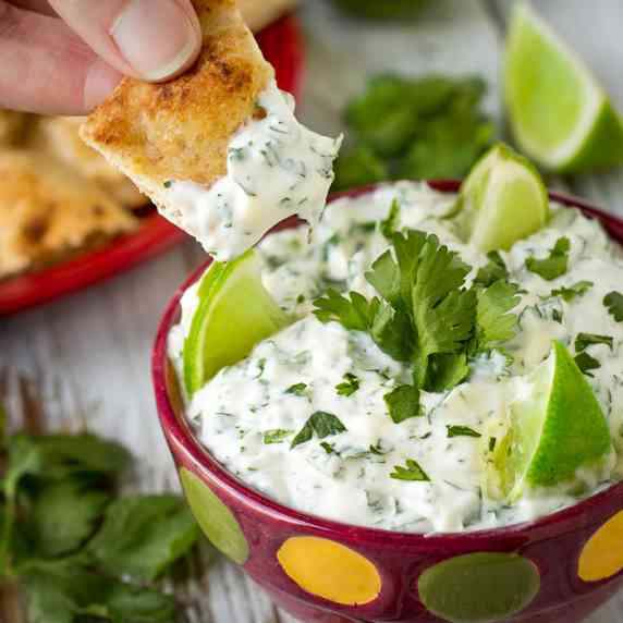 Close up angled shot of cilantro lime dip garnished with limes and cilantro in a red polka dot bowl.