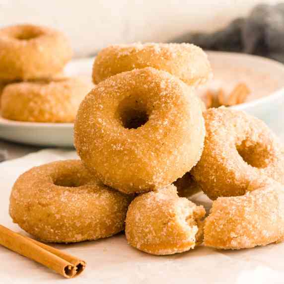 A stack of cinnamon sugar donuts on a white surface next to a cinnamon stick.