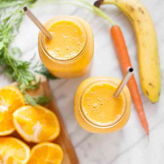 Top view of two bright orange cold buster smoothies in glass jars with metal straws on a counter.
