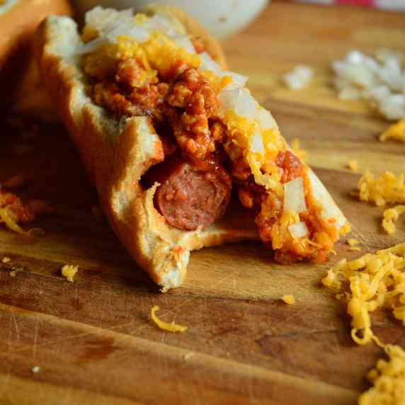 half eated coney dog on wood cutting board with chili, cheese and onions