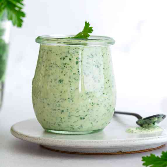 a jar of green cilantro sauce is placed on a white round plate