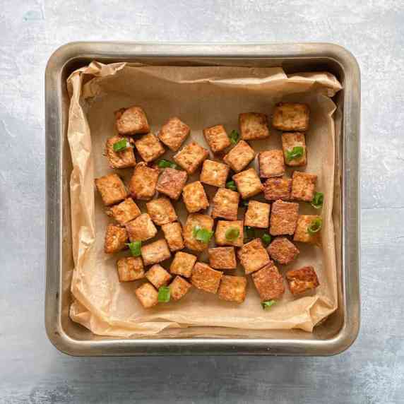 parchment-lined pan with crispy baked tofu garnished with scallions.