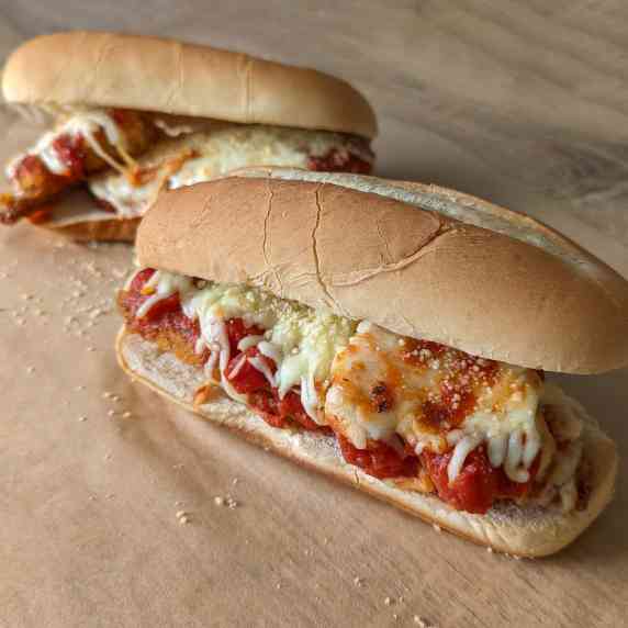 Two saucy, cheesy crispy chicken parm sandwiches on Italian sub rolls