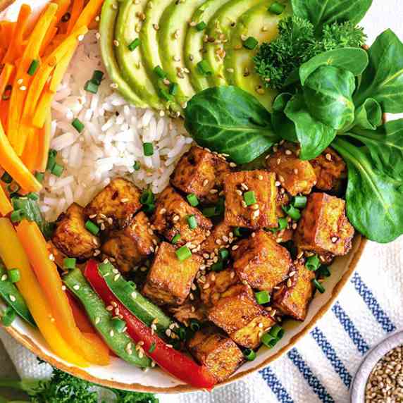 crispy tofu with sliced avocado, carrot, greens and bell pepper, served on a rice base