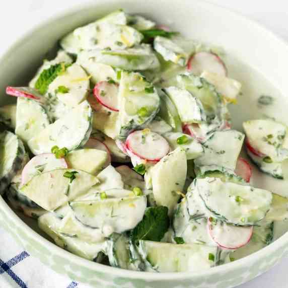 A bowl of sliced apple, cucumber and radishes covered in a creamy white dressing.