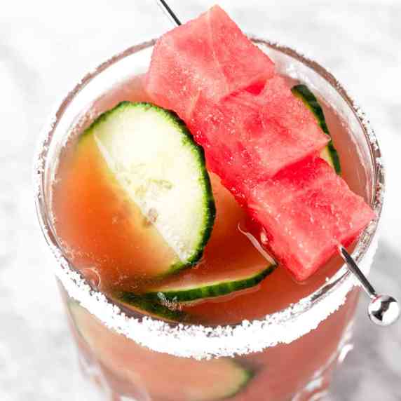 A cucumber margarita garnished with watermelon chunks and cucumber slices.