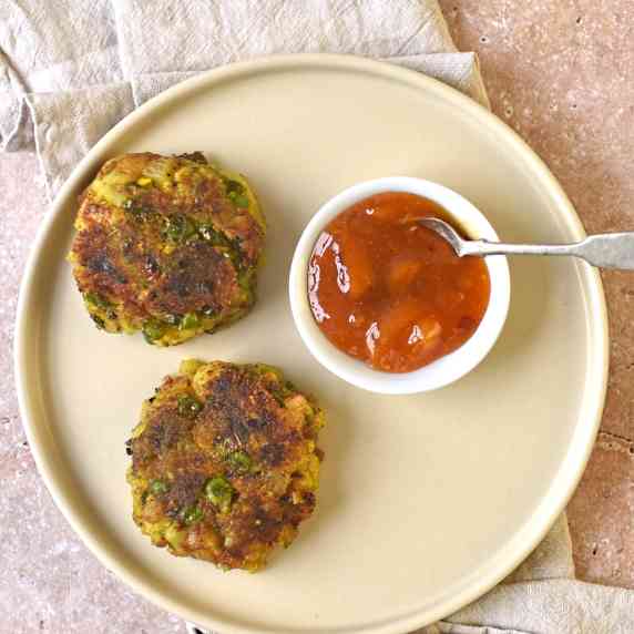 two vegan curried vegetable burgers accompanied by a small bowl of mango chutney