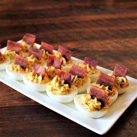 A white plate of deviled eggs garnished with bacon