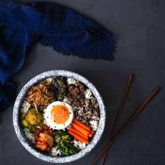 Bibimbap in a dolsot (stone bowl) with brown chop sticks on a gray surface.